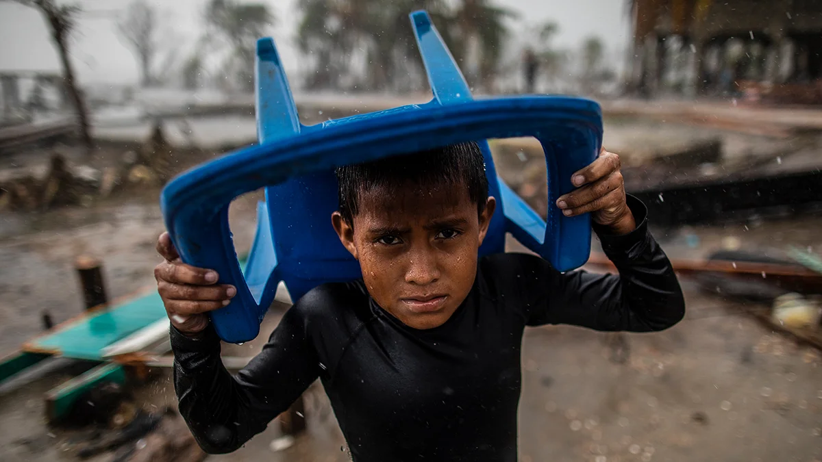 Am 17. November 2020 schützt sich in Bilwi, Nicaragua, ein Kind mit einem Plastikstuhl vor dem starken Regen und steht an der Stelle, an der einst sein Haus stand, nachdem es durch die starken Winde, Wellen und Regenfälle des Hurrikans Iota zerstört worden war.