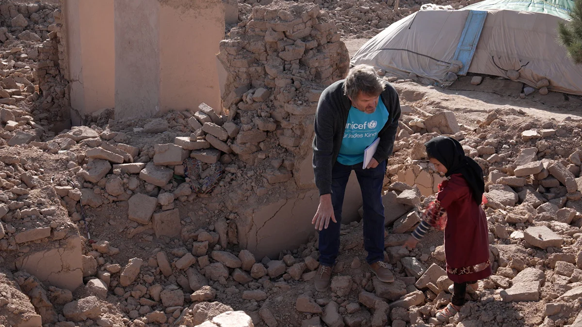   UNICEF Kommunikationschef Daniel Timme steht mit einem Mädchen inmitten der Trümmer ihres Hauses.